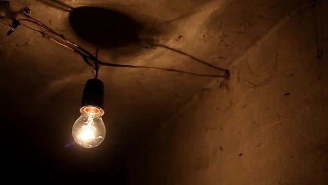 Old tungsten bulb. The incandescent lamp with a tungsten filament wobbles on the wire. Light from a light bulb. Light bulb close-up covered with cobwebs.