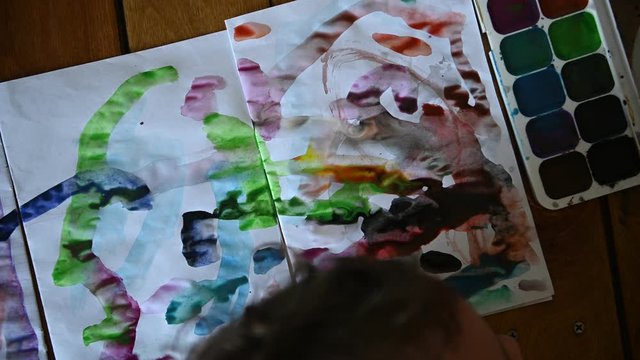 Little boy 4 years old draws with watercolors on a white sheet
