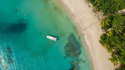 Aerial shot looking down onto boat in crystal clear aquamarine water and deserted white sandy beach