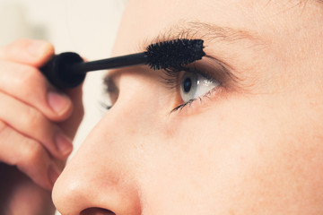 Beautiful young caucasian woman paints lashes with black mascara