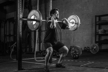 Fototapeta na wymiar asian strong athletic man having workout and bodybuilding with barbells weight front squat setting style in gym and fitness club in black and white