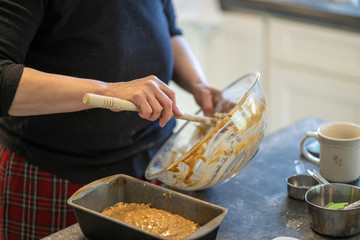 Bowl of cake bread batter in a big glass bowl with a wooden spoon being scraped into metal loaf pan.