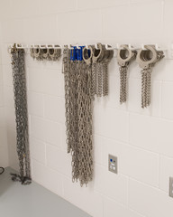 Handcuffs, chains, shackles hanging on hooks on block wall in Jail. Multiple sets hanging neatly in...