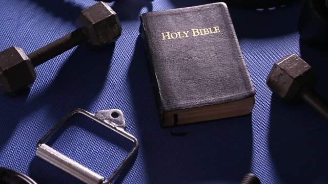 Bible Surrounded by Various Gym Equipment 