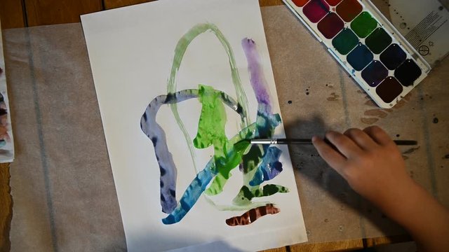 Little boy 4 years old draws with watercolors on a white sheet