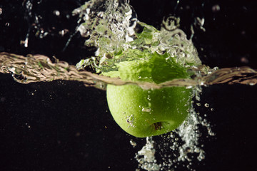 Green apple falling in water with splash on black background.