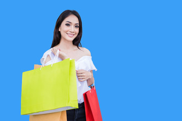 Beautiful asian young woman is standing holding shopping bags .She smile happiness in the shopping mall on blue background