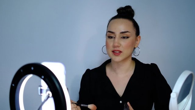 Attractive beauty blogger making online broadcast to her subscribers about makeup with phone in front of ring light, slow motion shooting beauty influencer vlog.
