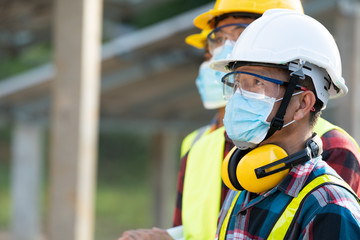 Workers wear protective face masks for safety working in Solar cell Farm through field of solar panels,Corona virus has turned into a global emergency.