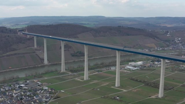 Hochmoselbr&uuml;cke High Moselle Bridge in Rhineland-Palatinate Germany with cars and trucks on a freeway highway cinematic panorama aerial drone shot on a sunny cloudy day 30p