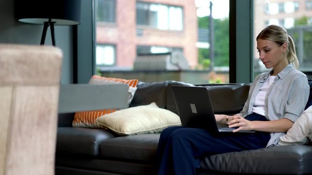 Young woman celebrating completed task at laptop computer sitting on comfortable couch and using wireless home internet.Hipster blogger doing shopping online on digital netbook in apartment
