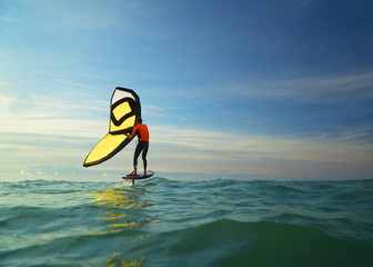 A man wingfoils in the sea on a summer's day, using a hand held inflatable wing and riding a...
