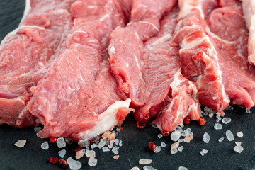Beef. Fresh raw beef steaks on a black slate plate. Raw ribeye steaks on a slate plate with salt and pepper. Steaks with spices on a black slate board.