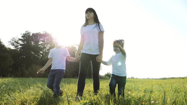 happy family teamwork mother, little brother and sister walk in the park nature holding hands slow motion video concept. mom, kids boy and girl lifestyle daughter and son hold hands go on green grass