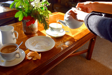 Pouring hot tea into a cup on wooden table background with bright light from sun, Traditional english tea in afternoon.