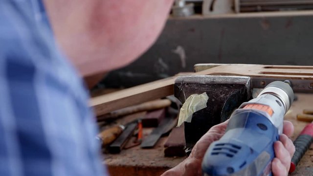 Luthier drills holes for tuning pegs in headstock of guitar. Madeira