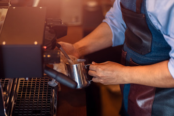 Barista steaming milk in the pitcher with coffee machine for  preparing to make latte art.