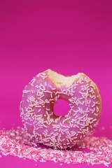 Donut pink.Baking and sweets. Pink bite donut on a pink sweet decor on a  fuchsia background.Sweet dough dessert.Donut with pink icing and white sugar decor.