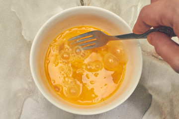 whips with a fork the development of an egg in a plate with pepper yolk on a marbled table. top view