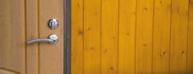 Modern chrome stainless steel door knob on a natural hardwood door with black wooden door frame. Concept for interior design and architecture.