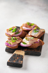 Smorrebrod, tapas or sandwich with onion and herring  on the cutting board.  Copy space