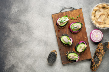 Smorrebrod, tapas or sandwich with onion, cucumber and herring  on the cutting board. Top view. Copy space
