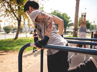 Handsome young man portrait training calisthenics with arms with tattoos and muscles on parallel bars in a street workout park on a sunny day with nature