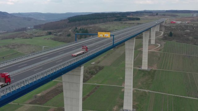 Hochmoselbr&uuml;cke High Moselle Bridge in Rhineland-Palatinate Germany with cars and trucks on a freeway highway cinematic inflow medium aerial drone shot on a sunny cloudy day 25p