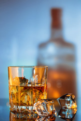 Glass of whiskey and ice against the background of bottle