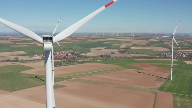 Rotating wings of  wind power plant producing renewable green clean engergy electricity in a wind farm on a sunny day, drone aerial cinematic rotating clops up shot, 30p