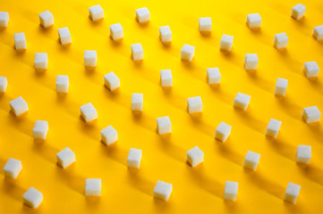 Fototapeta na wymiar Refined sugar cubes shot on a yellow background. Background for sweets, food and drinks.