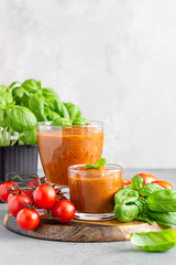 Summer homemade cold tomato cream soup in glass. Traditional Spanish soup gazpacho with basil. Grey concrete background.