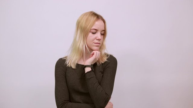 Young Blonde Woman In Black Sweater On White Background, Dreamy Girl Touches Her Chin And Thinks. The Concept Of Smart People, Intellectuals, Elite Of Society