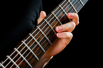 Seven-string electric guitar made of dark wood and human hands, shot on a dark background....