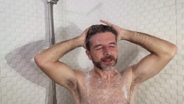 young attractive and happy man with beard taking a shower at home washing his hair with shampoo cheerful enjoying the morning shower in wellness and hygiene concept