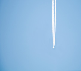 A plane is flying in the blue sky at high altitude. And leaves a white line behind