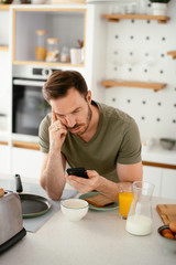 Fototapeta na wymiar Handsome man preparing breakfast at home. Young man using the phone in kitchen.