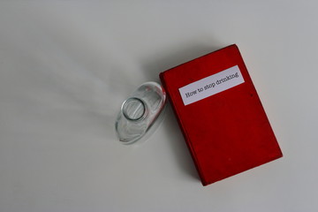 Selective focus on old red book title How to stop drinking placed on white wooden table next to empty glass bottle, high angle view, resolution concept 