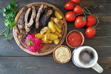 Beer in a white clay mug and traditional snacks on a rustic table - grilled ribs, slices of baked potatoes, sauerkraut. German cuisine.