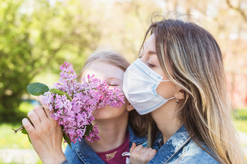 Obraz premium Mom and daughter sniffing a lilac on the street. Quarantine quit concept