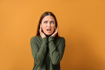 Young woman suffering from loud noise on color background