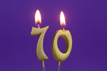 Golden burning birthday candle on blue background, number 70