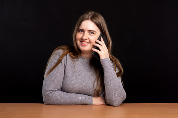 young girl with long hair is talking on the phone at the table on a black background. smile. place for text. isolate