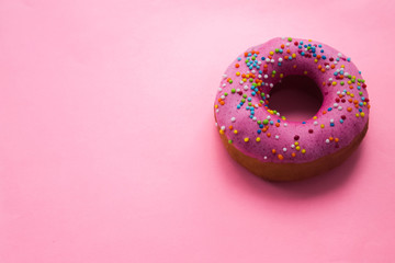 Homemade circle donut with pink icing and rainbow sprinkles on the trendy soft pink background situated on the right side. Free copy space. Doughnut pastry.