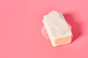 Foam bubbles and brick of soap on pink background. Cleaning service. Concept of hygiene, washing, disinfection