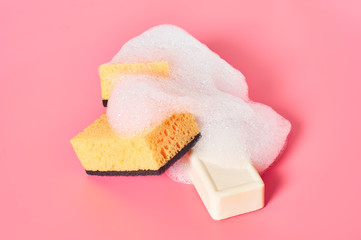 Brick of soap with foam bubbles near sponge on pink background. Washing, cleaning concept