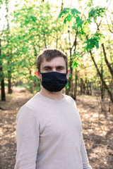young man in a medical mask in the park on a background of nature. quarantine difficulties. close-up portrait. European appearance. infection protection