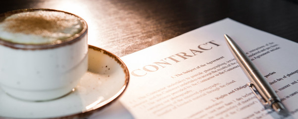 cup of coffee with foam, ballpoint pen, blank contract on a wooden table