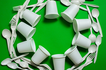 disposable forks, spoons and glasses of corn starch on a green background. biodegradable cookware...