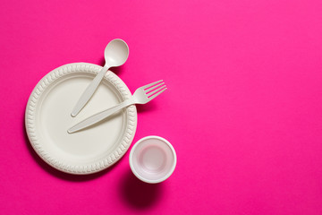 disposable biodegradable fork, spoon, glass and plate of corn starch on a pink background....